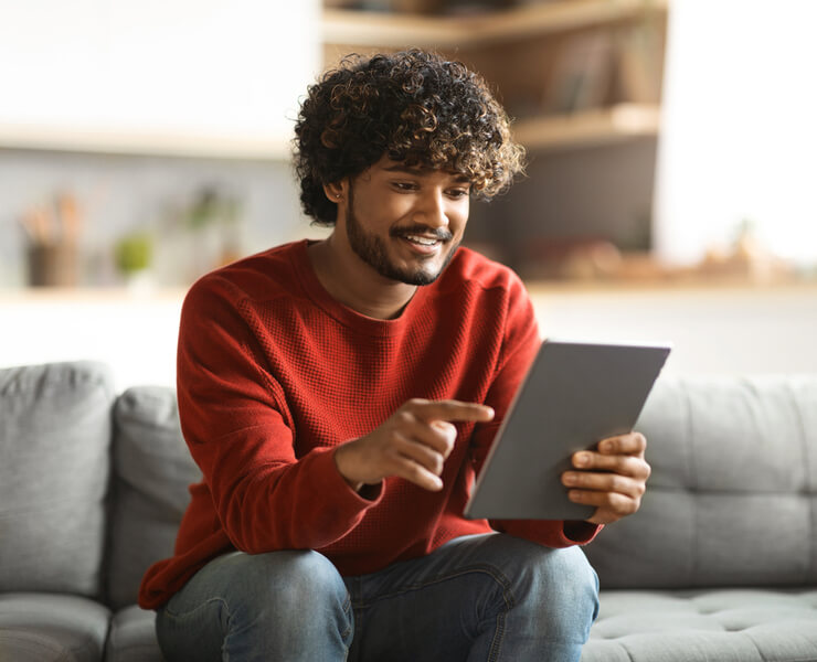 A person sitting on a couch and looking at a tablet.